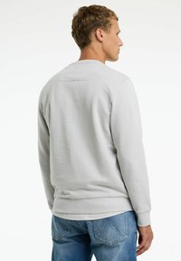 Sudadera gris claro con textura acanalada, escote redondo y un pequeño parche en la parte trasera. Usada con jeans de mezclilla azules.