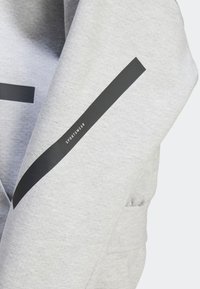 Tissu gris clair avec une bande diagonale noire arborant le mot « SPORTSWEAR » en petites lettres blanches.