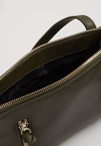 Borsa in pelle verde oliva con zip superiore, dotata di hardware in tonalità oro e fodera interna nera. Design compatto con manico laterale.