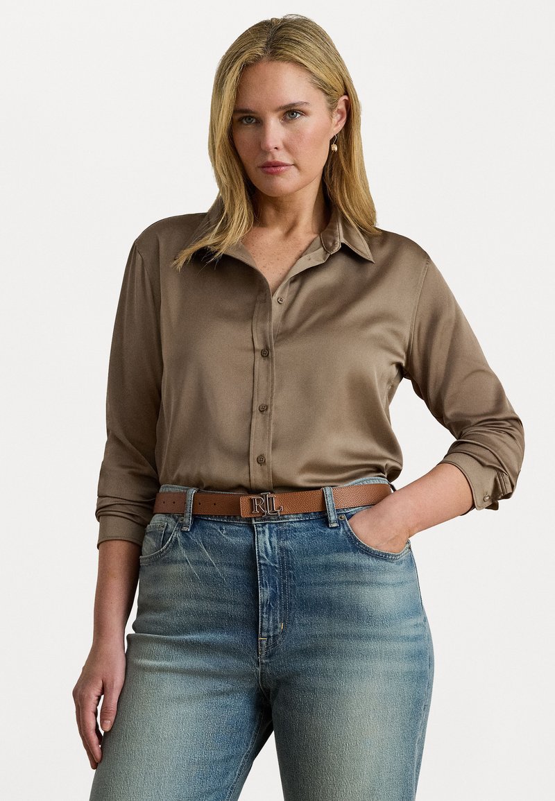 Bruine satijnen blouse met lange mouwen en knopen aan de voorkant, gecombineerd met lichtblauwe spijkerbroek en een tan riem met een emblematische gesp.