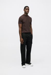 T-shirt de algodão castanha com mangas curtas e um gráfico no peito, combinada com calças cargo pretas e ténis pretos com sola branca.