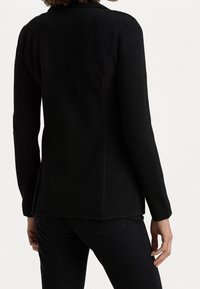 Černý blazer s dlouhými rukávy, vyrobený z texturované tkaniny, s rovný střih a jemným detailem bočního švu, bez viditelných zapínání.