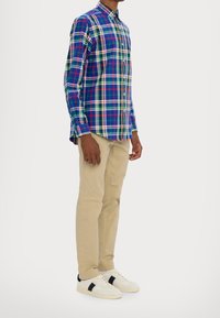 Flerfärgad rutiga skjorta med blå, grön, röd och vita mönster, tillsammans med beige byxor och vita sneakers med svarta accenter.