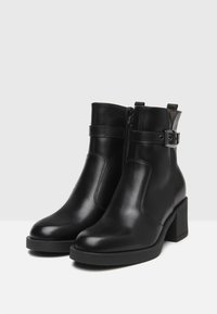 Bottes noires en cuir jusqu'aux chevilles avec un talon bloc rectangulaire, fermeture éclair latérale et une sangle décorative avec une boucle en argent.
