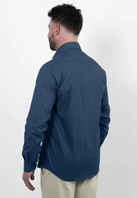 Marineblaues Hemd mit Knopfleiste aus einem glatten Stoff, mit langen Ärmeln, einem spitzen Kragen und einem abgerundeten Saum, sowie subtilen Texturdetails.