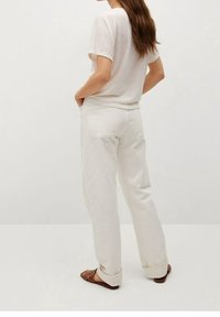 Camiseta blanca ligera de manga corta, combinada con pantalones blancos holgados con bolsillos traseros, utilizados con sandalias planas marrones.