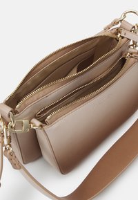 Sac bandoulière en cuir beige avec deux compartiments principaux zippés et quincaillerie métallique dorée, présenté ouvert pour révéler les poches intérieures.