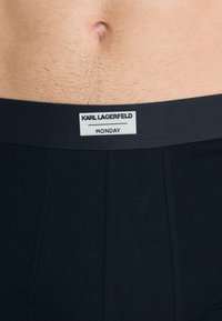 Fekete boxeralsó, puha derékpánttal, amelyen a "KARL LAGERFELD MONDAY" logófelirat található, rugalmas anyagból készült.