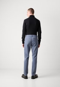 Un suéter negro de cuello alto se combina con pantalones de color azul claro. Los pantalones cuentan con dos bolsillos traseros y están hechos de una tela suave. Unos zapatos negros completan el look.