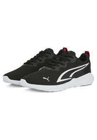 Zapatos deportivos negros fabricados con material de malla, con una parte superior texturizada, una entresuela blanca y un acento rojo en el talón. Presenta un logotipo y cordones.