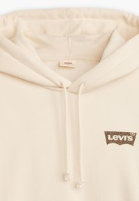 Beige hoodie med dragsnören. Mjukt tyg med en brun Levi's-logotyp som har ett leopardmönster på framsidan.