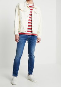 Hvid denimjakke, rød- og hvidstribet T-shirt, blå skinny jeans og hvide sneakers. Casual outfit med kontrasterende farver og lag.