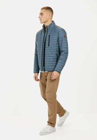 Blauwe gewatteerde jas met hoge kraag, ritssluiting aan de voorkant en zwarte accenten. Gepaard met beige broek en witte sneakers. Eenvoudig ontwerp.