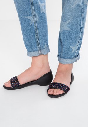 Feet wearing black open-toe sandals with multicolored beads, paired with rolled-up blue jeans featuring a star pattern.