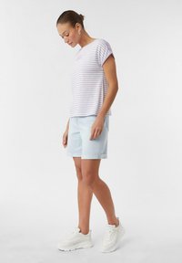 Wzorzysty t-shirt w kolorze lawendowym i białym z podwiniętymi rękawami, w komplecie z jasnoniebieskimi szortami dżinsowymi. Model ma na sobie białe sneakersy.