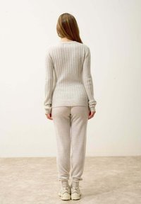 Jasnoszary sweter prążkowany z długimi rękawami, połączony z miękkimi szarymi dresami i jasnymi sneakersami, wyeksponowany od tyłu na neutralnym tle.