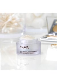 Crema per gli occhi AHAVA in un barattolo trasparente satinato con un coperchio bianco. L'etichetta presenta testo marrone e blu. Il prodotto appare cremoso con un colore chiaro.