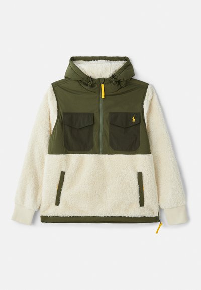 Ανορακ τζάκετ με κουκούλα, πάνω μέρος από πράσινο νάιλον, κάτω μέρος από κρεμ φλις, διπλές θήκες στο στήθος και λεπτομέρεια με φερμουάρ σε κίτρινο χρώμα.