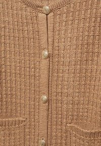Sweter z dzianiny w ciepłym odcieniu brązu, z fakturowanym wzorem, czterema złotymi guzikami i dwiema kieszeniami z przodu.