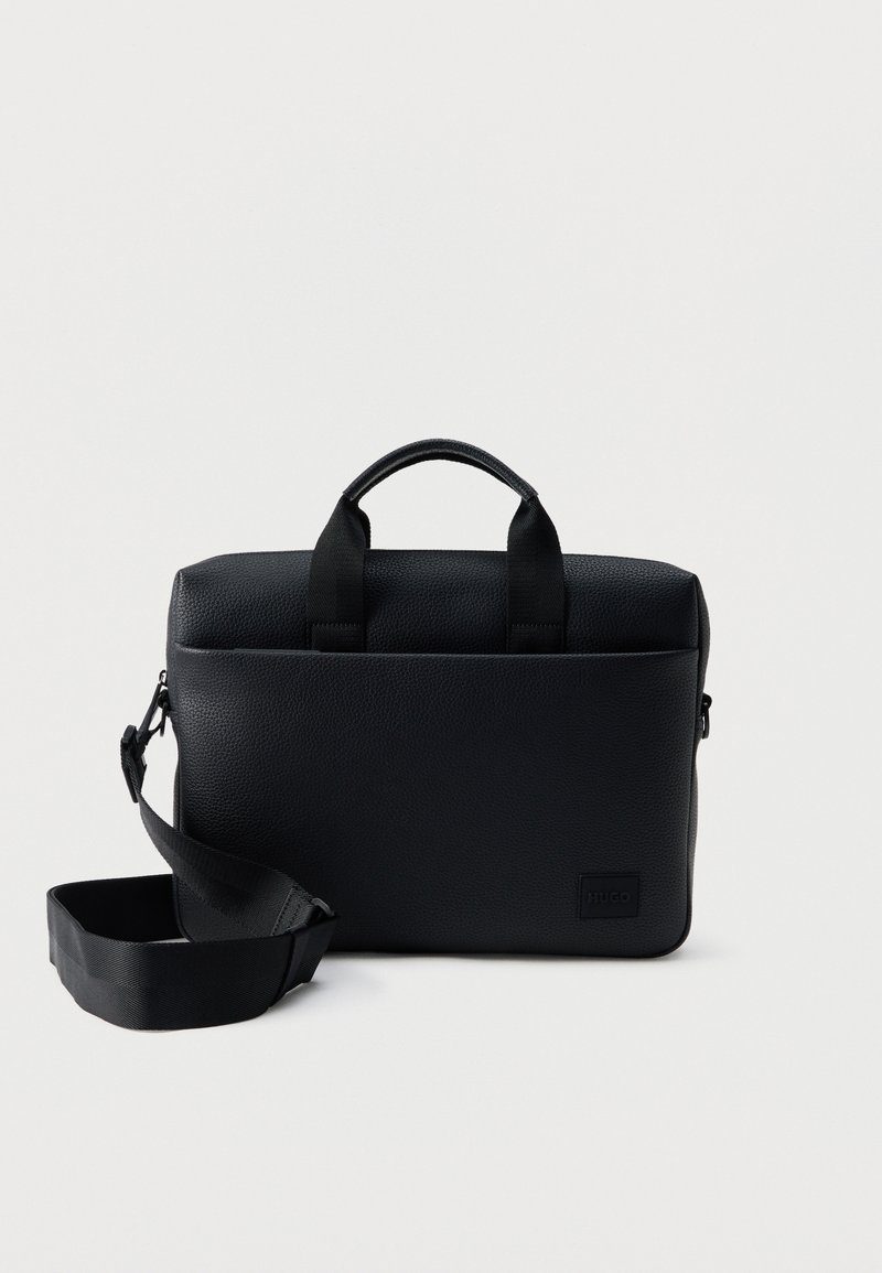 Mallette en cuir noir texturé avec poignées supérieures et bandoulière réglable, posée sur un fond blanc uni.