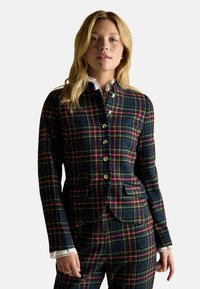 Plaid blazer in navy, green, and red tones, featuring gold buttons, tailored fit, and side pockets, paired with a white collared shirt.