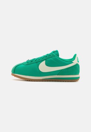 Lage groene sneaker met witte Nike-swoosh, gumzool en veters aan de voorkant, zijaanzicht op een effen achtergrond.