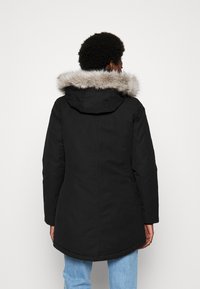 Giubbotto parka nero con cappuccio foderato in pelliccia, caratterizzato da un orlo leggermente curvo e maniche lunghe, realizzato in un materiale liscio e resistente all'acqua.