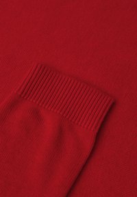 Czerwony sweter z dzianiny z ribbowanym mankietem, gładką fakturą i równym ściegom. Materiał jest miękki i lekko elastyczny dla wygody.