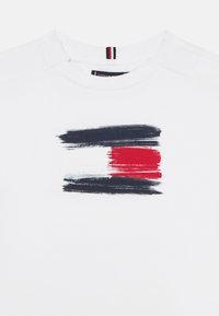 White cotton t-shirt featuring a horizontal brushstroke design in navy, white, and red across the chest. Round neckline detail visible.