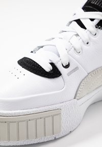 Białe skórzane sneakersy z czarnymi i szarymi akcentami, teksturowana podeszwa, okrągły czubek i płaskie sznurówki, z perforowaną detalizacją na cholewce.