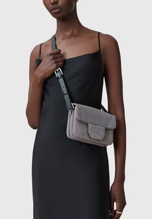 Borsa a tracolla grigia in ecopelle testurizzata con chiusura a pattina e tracolla nera regolabile, indossata su un vestito di satin nero.