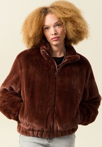 Brązowa kurtka bomberka z sztucznego futra z wysokim kołnierzem, zamkiem z przodu i elastycznym wykończeniem. Miękka tekstura i luźny krój odpowiedni do codziennego noszenia.
