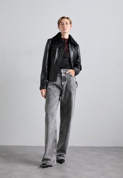 Black leather jacket with a wide collar, paired with high-waisted, loose gray jeans. Model stands against a light gray background.