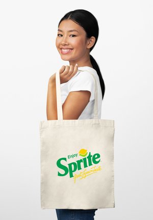 Borsa in tela di colore naturale con il logo di Sprite in verde e giallo, tenuta da una persona che indossa una maglietta bianca.