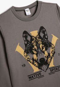 Szary sweatshirt z czarnym i złotym nadrukiem wilka, z napisem "NATIVE SPIRIT" oraz wyróżniającym się elementem projektowym w postaci skrzyżowanych liter.