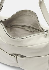 Borsa in pelle bianca con scomparto principale con zip e tasca interna. Texture morbida con design curvo e dettagli di cucitura a contrasto.