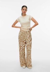 Haut beige cintré à manches courtes associé à un pantalon à jambes larges à rayures zébrées marron et blanc. Texture de tissu lisse avec une coupe décontractée.