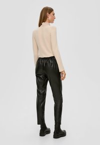 Beige enganierter Rollkragenpullover mit langen Ärmeln, kombiniert mit schwarzen Jogginghosen aus Kunstleder und schwarzen Knöchelstiefeln.