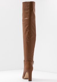 Bota de cuero marrón hasta la rodilla con un diseño elegante, tacón alto y detalle de cremallera lateral. Textura suave y forma aerodinámica.