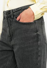 Czarne dżinsy o wysokim stanie z teksturowanym wykończeniem, z przednią kieszenią, zapięciem na guzik i delikatnymi detalami w szyciu.