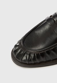 Μαύρο δερμάτινο παπούτσι με στρογγυλεμένη μύτη, που διαθέτει πλισέ σχεδιασμό κατά μήκος του μπροστινού μέρους και λεία, γυαλιστερή επιφάνεια.