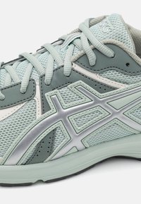Shoe atlético verde-claro com parte superior de malha, detalhes prateados e sola acolchoada. Apresenta sobreposições padronizadas e design com cordões.