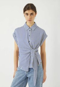 Camicia a maniche corte a righe blu e bianche con colletto e dettaglio annodato sul davanti, realizzata in un tessuto leggero.