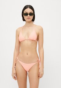 Rosa ribbad bikiniuppsättning med trekanttopp och justerbara knytbitar. Minimalistisk design med tunna remmar och slät textur.