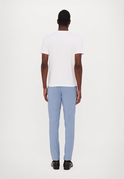 Weißes T-Shirt mit kurzen Ärmeln, hellblaue Hose und schwarze Schuhe, von hinten betrachtet. Glattes Material und taillierter Schnitt.