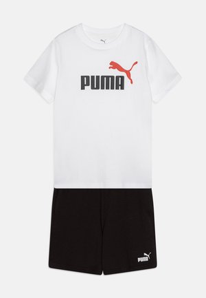 T-shirt bianca a maniche corte con logo "PUMA" nero e rosso, abbinata a pantaloni neri con logo "PUMA" bianco sull'orlo.