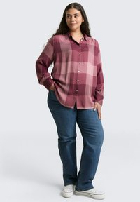 Geruite shirt in tinten van bordeauxrood en roze, lange mouwen met knoopmanchetten, relaxte fit, gecombineerd met blauwe jeans en witte sneakers.