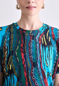Multifarvet T-shirt med korte ærmer, der har et livligt mønster af blå, rød, grøn og sort med teksturerede detaljer og en rund halsudskæring.