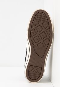 Hnědá gumová podrážka tenisky s diamantovým vzorem. Obsahuje béžový postranní díl a částečný černý textilní svršek.