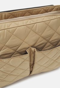 Zaino beige trapuntato con due tasche esterne, texture liscia e doppie aperture con zip. Progettato con una forma strutturata.